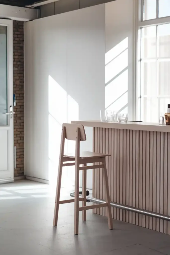 Minimalist Scandinavian Bar Stool: Generate an image of a minimalist Scandinavian-style bar stool made of light wood and simple lines, placed in a clean and airy home bar with neutral colors and natural light streaming in.