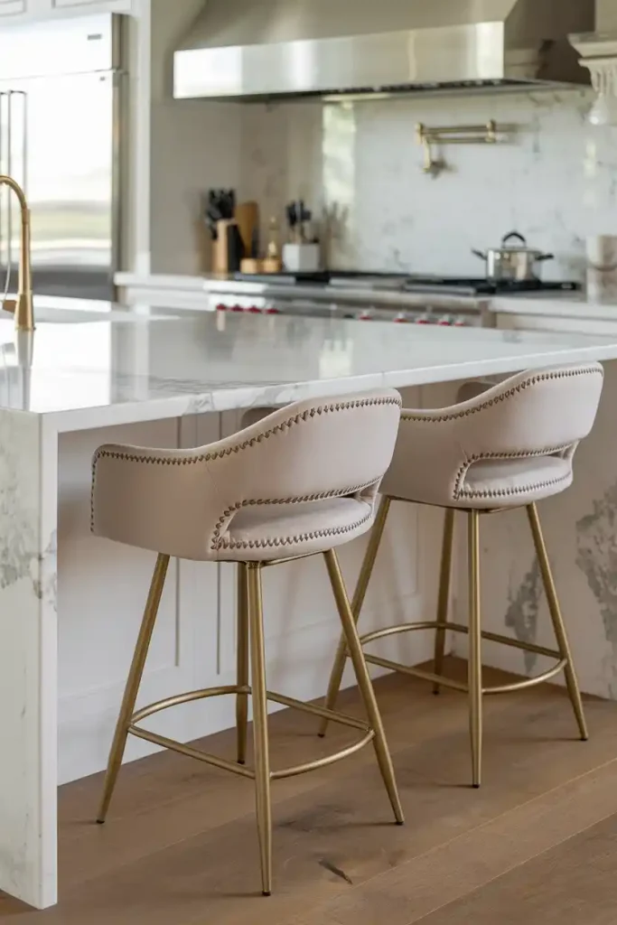 a sophisticated kitchen island with marble countertops, complemented by elegant upholstered bar stools in a soft fabric, featuring intricate stitching.