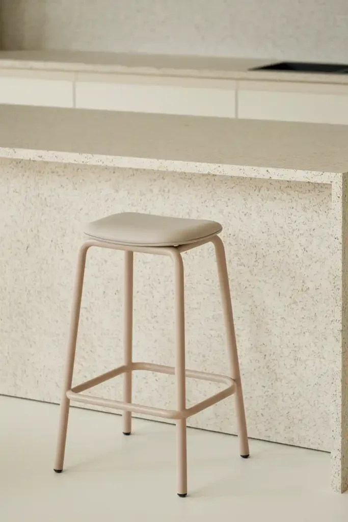 Minimalist Design: Generate an image of a minimalist bar stool with a simple silhouette and neutral upholstery, set against a light-colored granite countertop in a bright, airy kitchen.