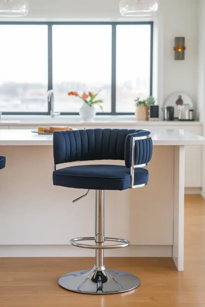 Swivel Bar Stool: Create an image of a stylish swivel 36-inch bar stool featuring a chrome base and a plush seat in navy blue, set at a modern kitchen island with pendant lighting above.