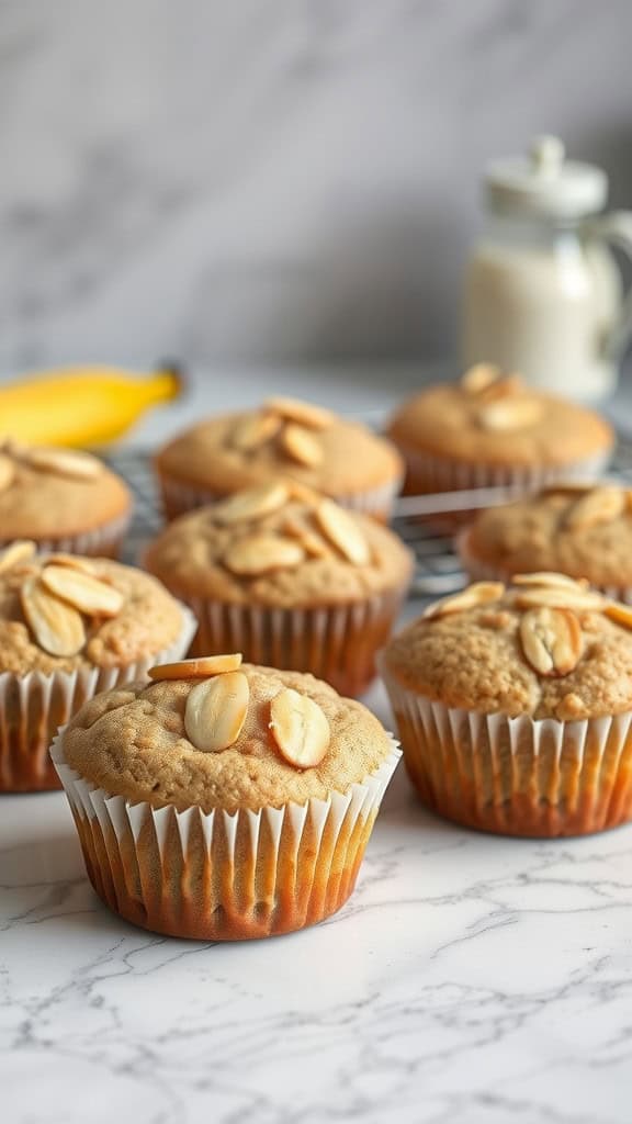 A close-up of freshly baked almond flour banana muffins on a marble surface, topped with sliced almonds, with a banana and a jar of milk in the background.