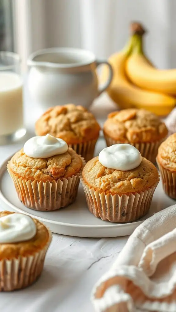 A plate of homemade yogurt banana muffins topped with cream, with bananas and a glass of milk in the background.