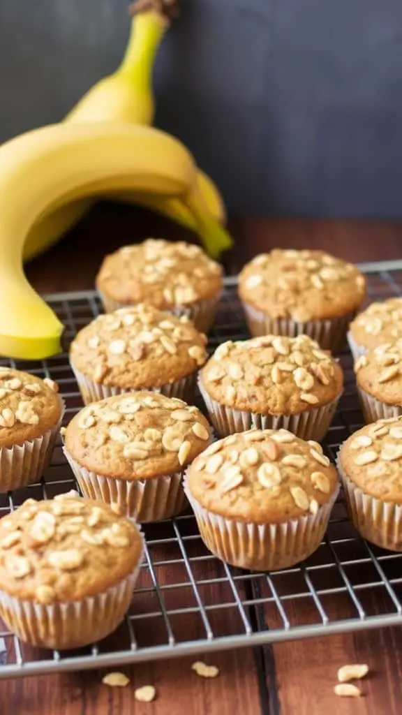 Golden muffins with visible oats and banana slices, placed on a marble countertop with a blender in the background.
