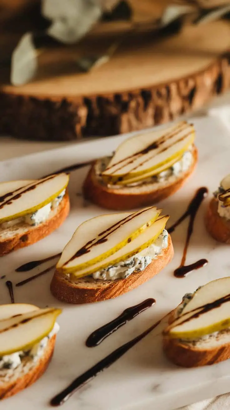 Crostini topped with blue cheese and pear slices, drizzled with balsamic reduction on a marble platter.