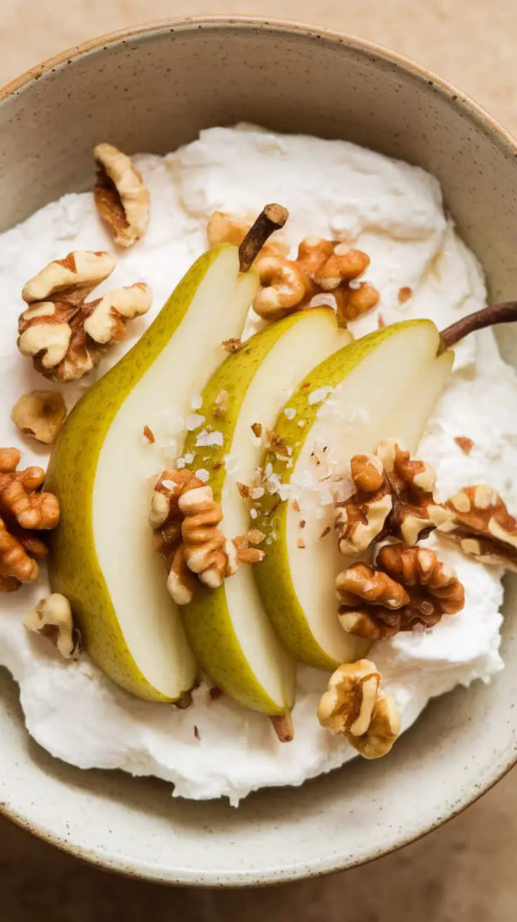 A bowl of sliced pears on creamy base topped with walnuts and sea salt